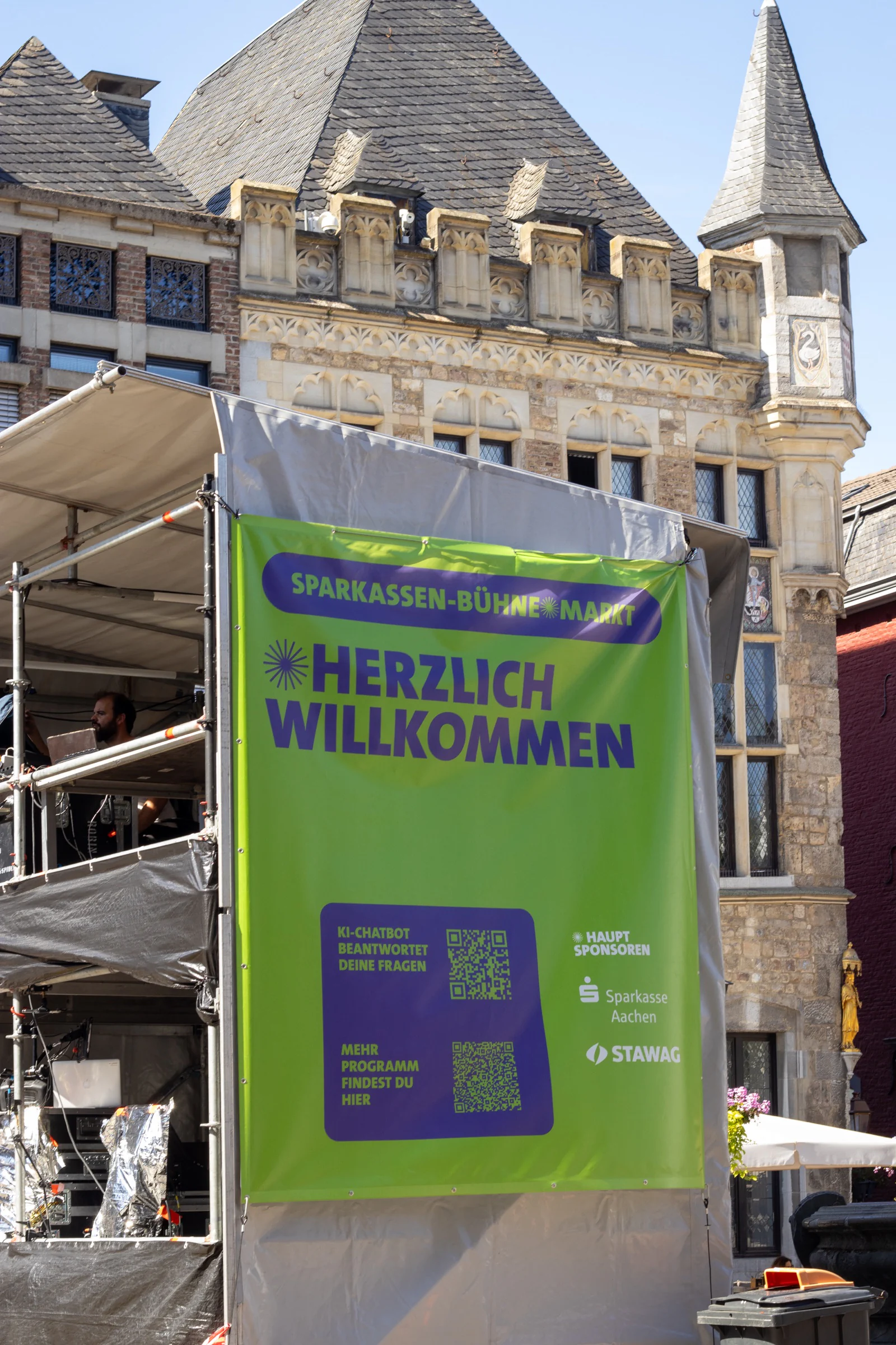 Grünes Herzlich-willkommen-Banner der Sparkassen-Bühne Markt mit KI-Chatbot-QR-Code vor historischer Fassade