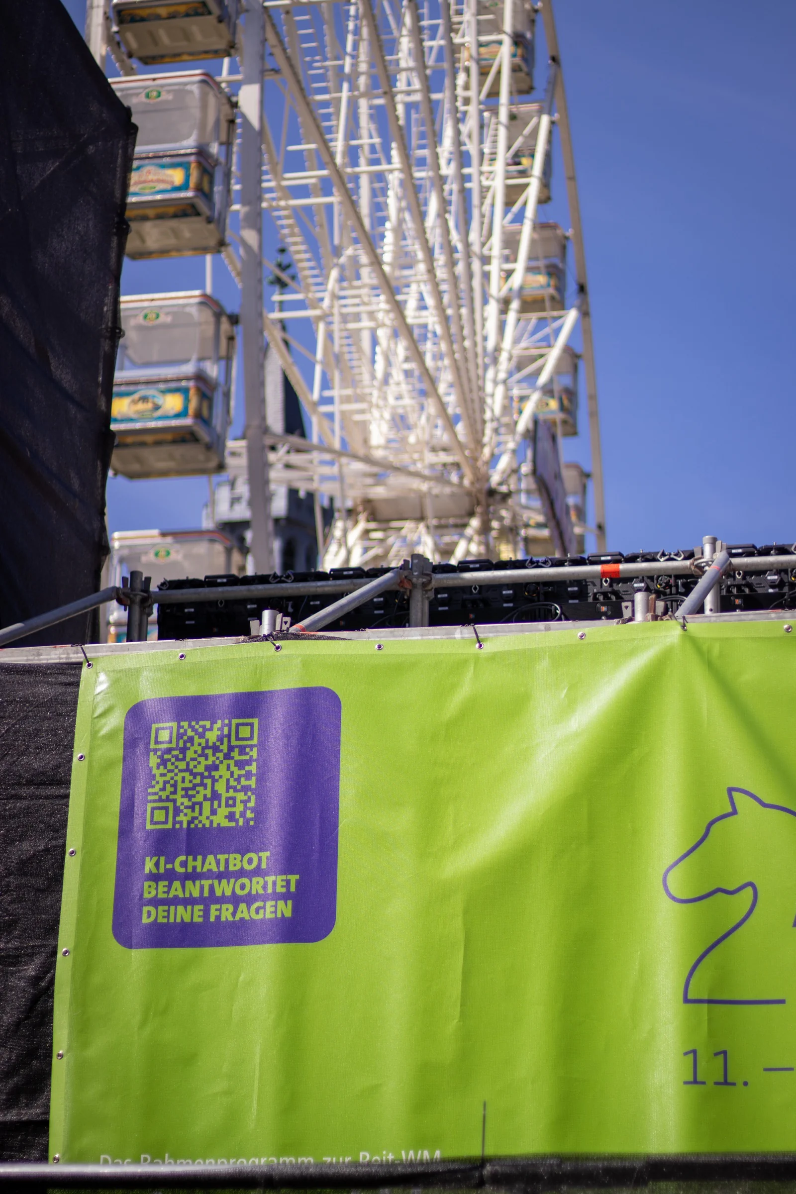 Riesenrad und grünes Aachen-WM-Special-Banner mit QR-Code zum KI-Chatbot