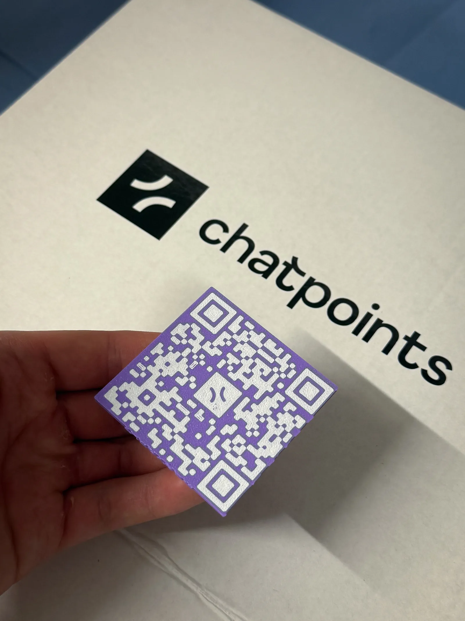 Eine Hand hält einen violetten 3D-gedruckten QR-Code-Chip von chatpoints
